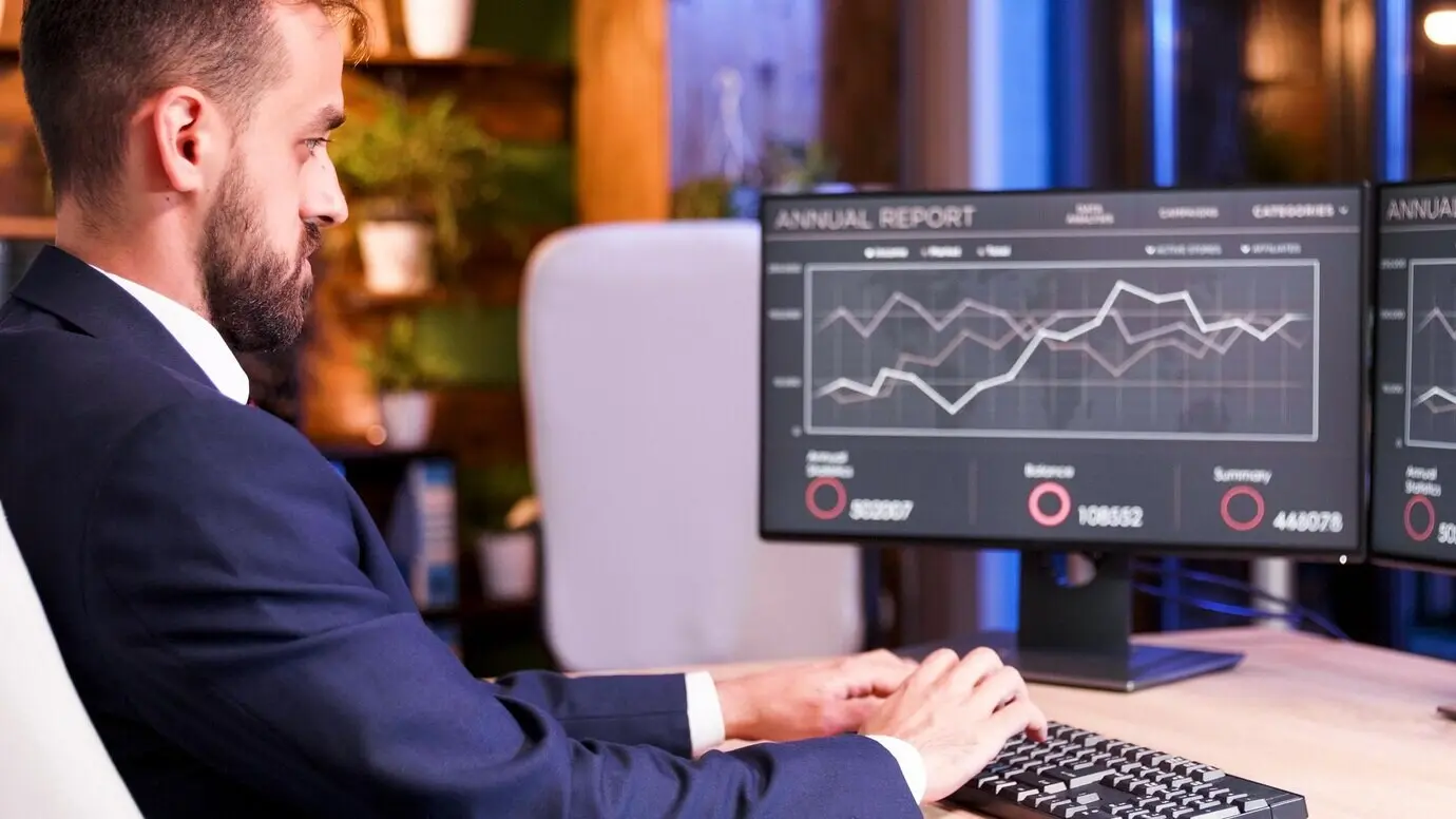 Крупный план бизнесмена, который патчит что-то на клавиатуре; на мониторе — графики.