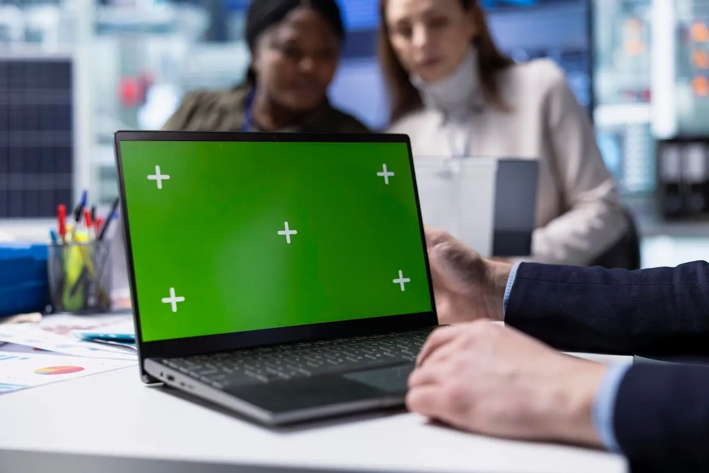 Сотрудник завода работает за макетным ноутбуком рядом с руководителями, обсуждающими стратегии.